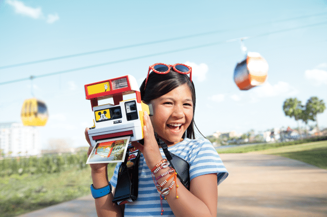 A guest poses with a camera in front of the Disney Skyliner