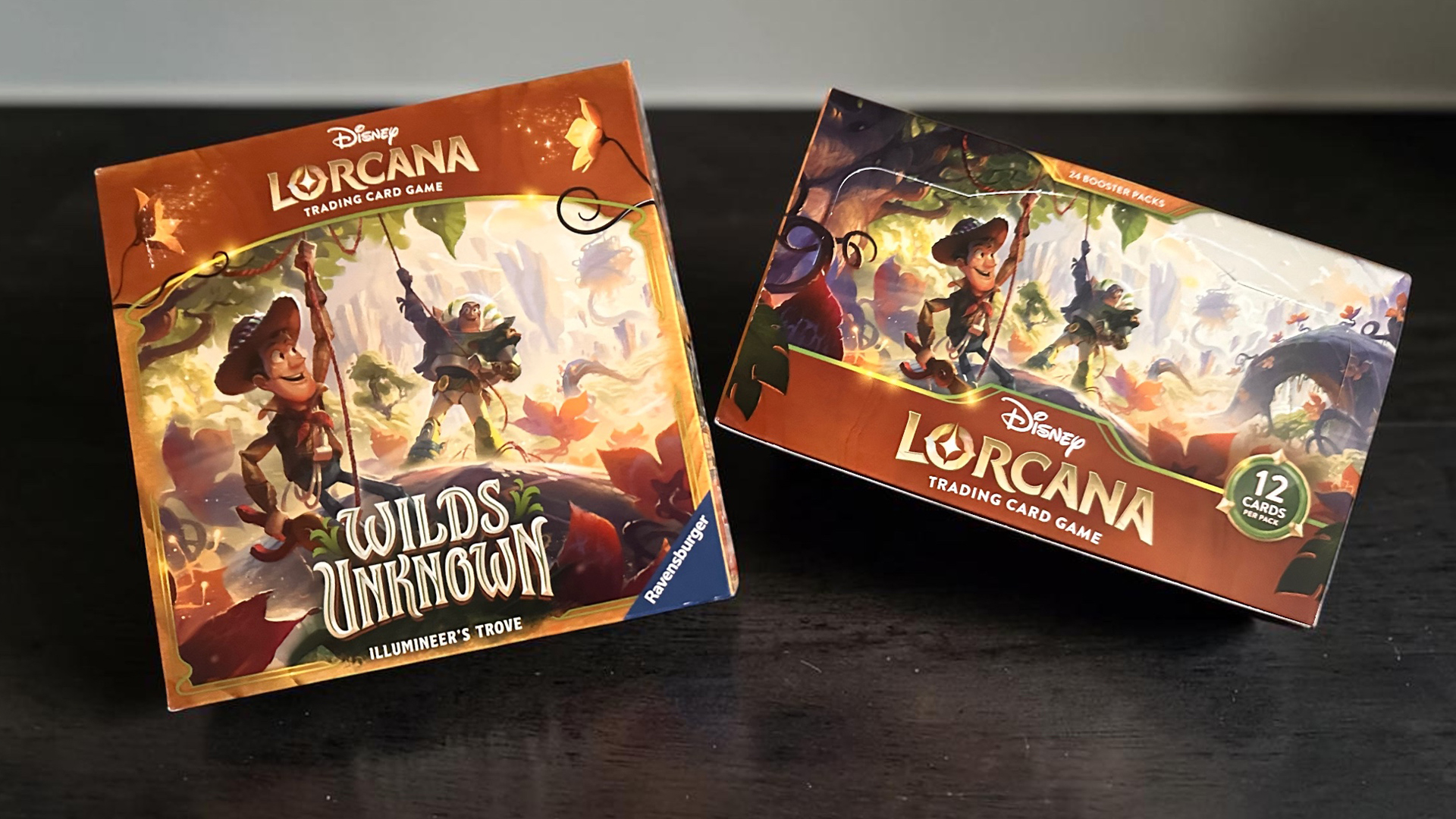 26EPCFoodWineDatesAnnouncedSocialv3bu | The Main Street Mouse Two Disney Lorcana trading card game boxes sit on a dark wooden surface with colorful fantasy artwork and character illustrations visible on both boxes The left box reads Wilds Unknown Illumineers Trove The right box shows a 12 Cards per Pack badge and Lorcana branding