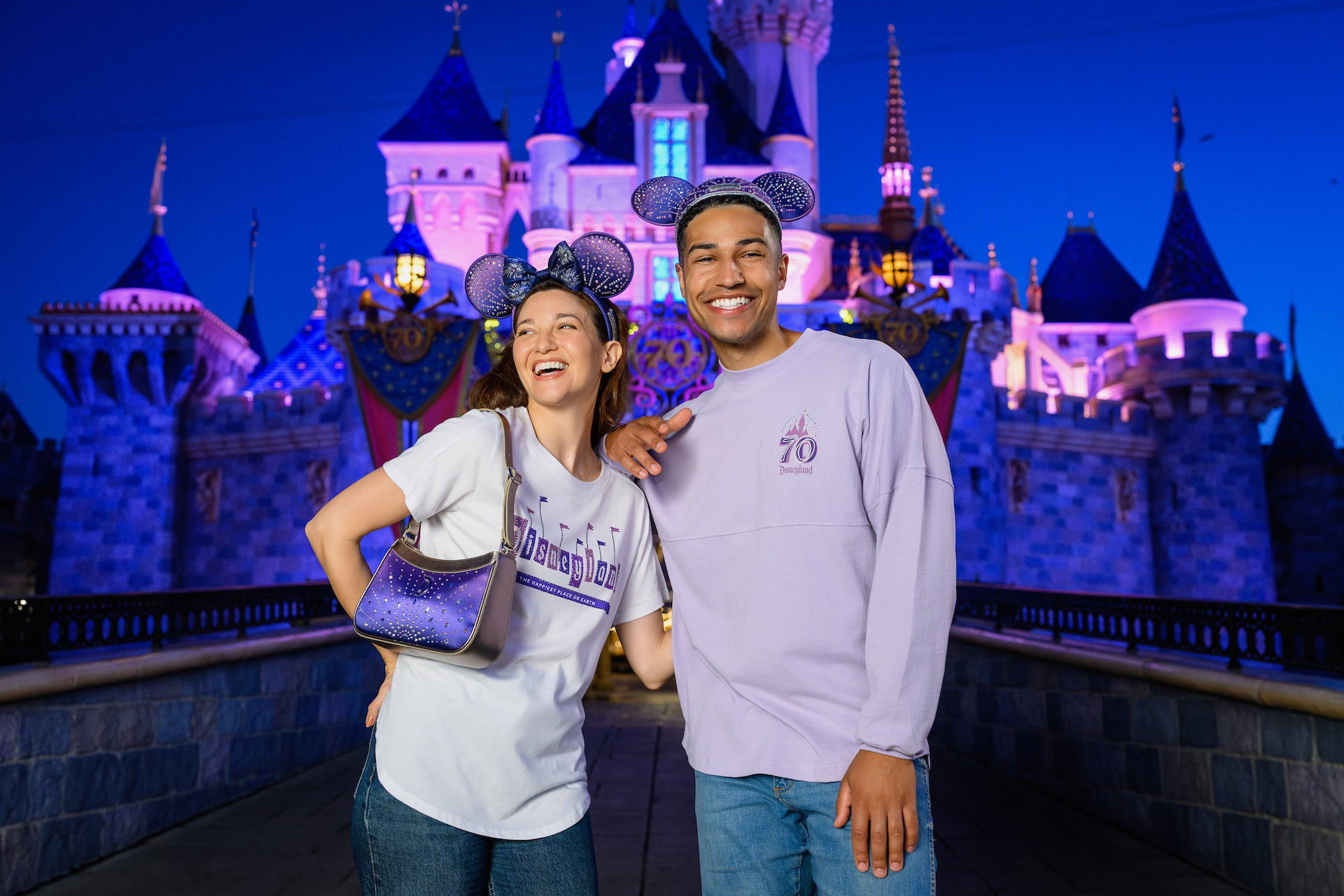 2026DLRFinaleMerchCollection6 | The Main Street Mouse Two Friends Wearing Lavender Shirts and Minnie Ears Pose in Front of a Lit Castle at Disneyland