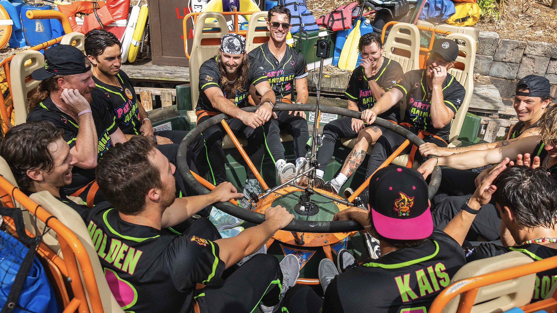 Group of Friends in Neon trimmed Black Shirts Around a Circular Steering Wheel on a Colorful Raft Smiling Together