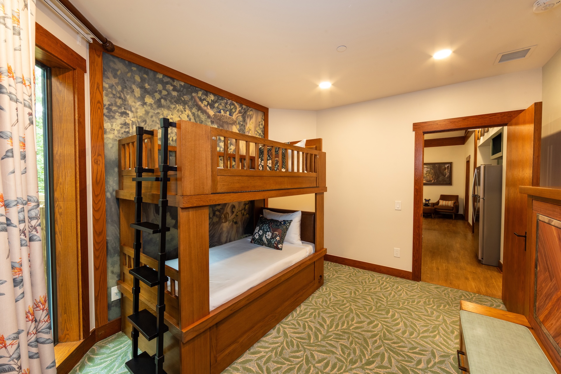 2026DVCReimaginedTreehouseVillas11 | The Main Street Mouse Wooden Bunk Bed with Metal Ladder in a Warmly Lit Room Green Patterned Carpet and a Doorway to a Living Areakitchen Beyond informative