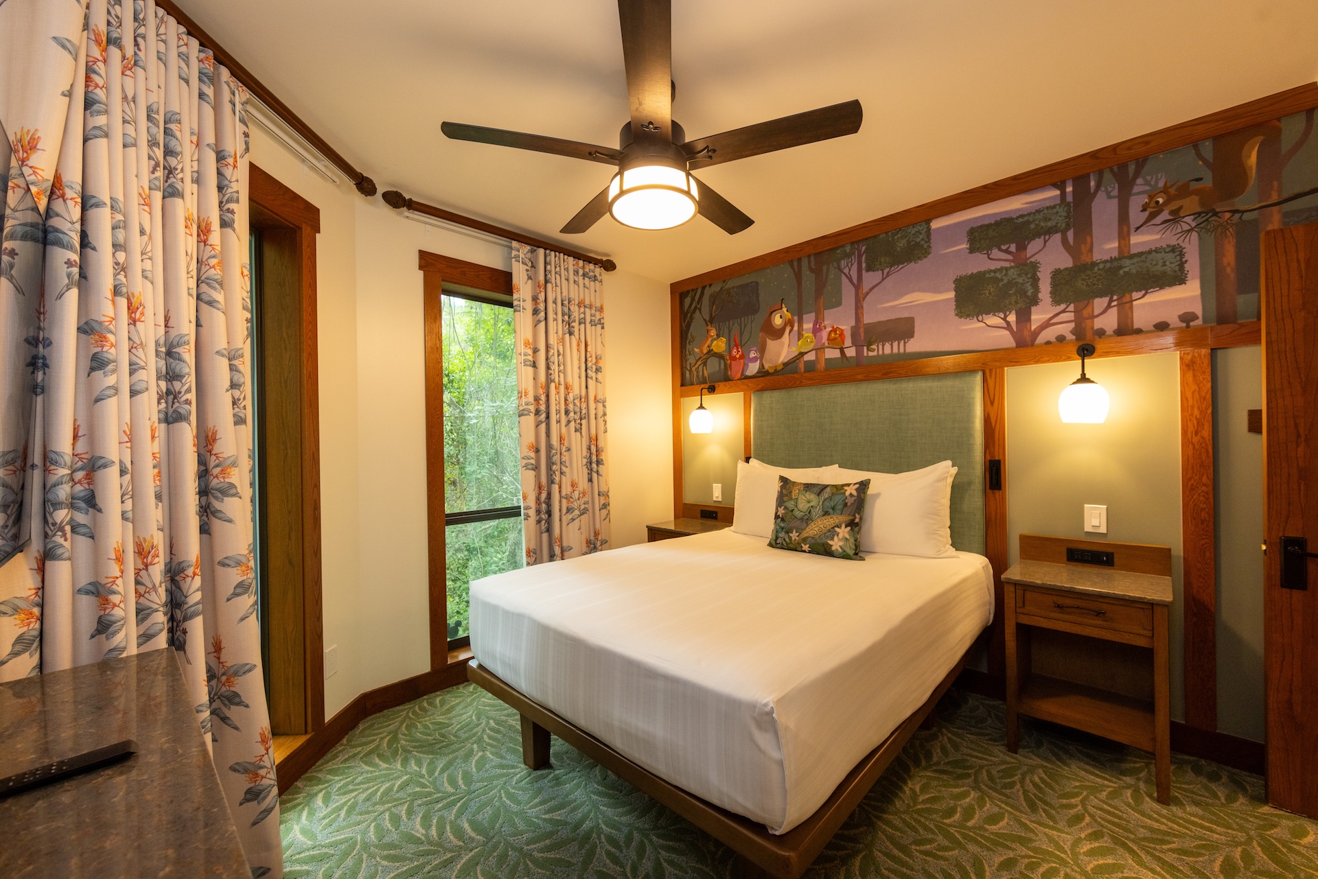 2026DVCReimaginedTreehouseVillas13 | The Main Street Mouse Queen Bed in a Forest themed Hotel Room with a Mural Above the Headboard Two Nightstands and Warm Lighting from Wall Lamps