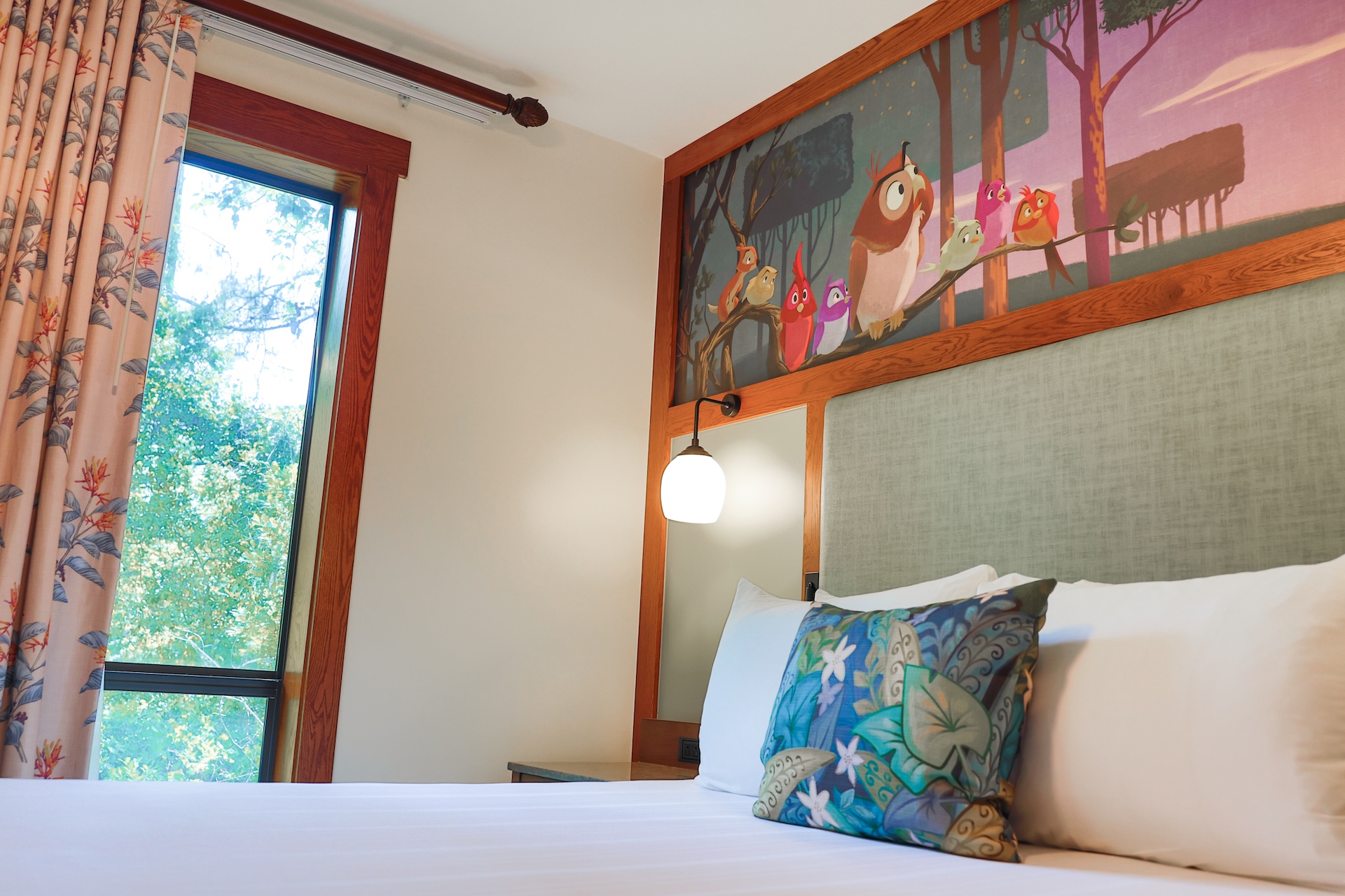 2026DVCReimaginedTreehouseVillas18 | The Main Street Mouse Hotel Bedroom with a Wooden Headboard White Bedding and Colorful Patterned Pillows in Front of an Owl Mural on the Wall
