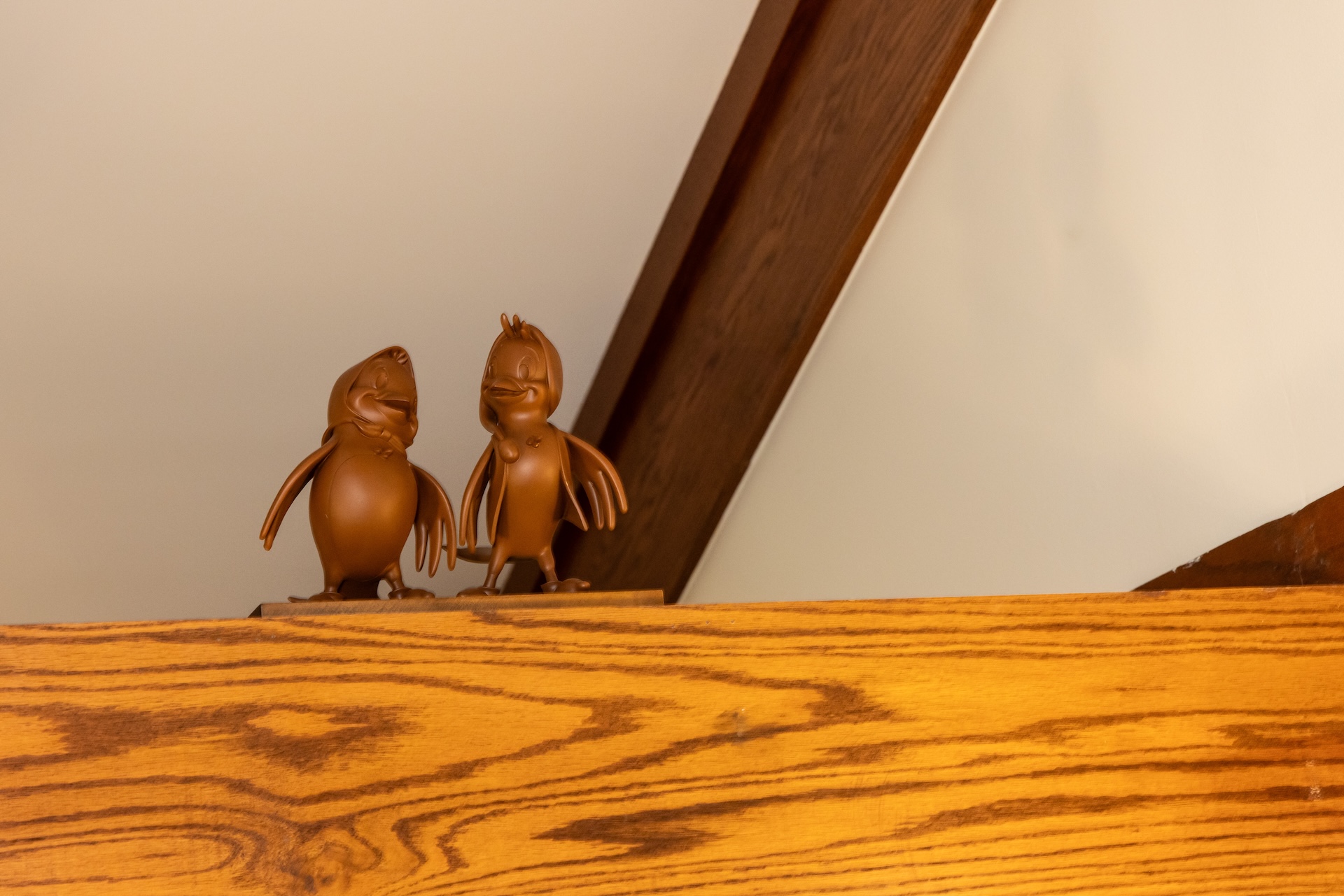 2026DVCReimaginedTreehouseVillas6 | The Main Street Mouse Two Brown Cartoon Duck Figurines Perched on a Wooden Shelf Against a Beige Wall with a Curved Dark Wood Beam in the Background