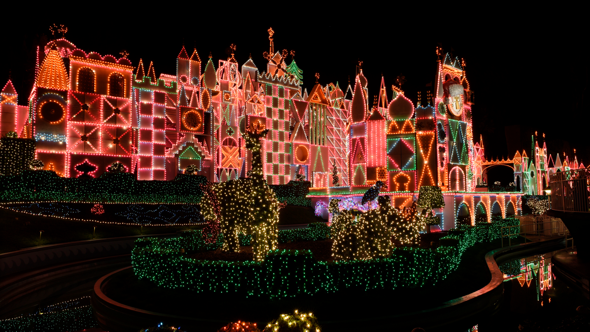Night View of a Castle shaped Holiday Light Display with Multicolored Neon Outlines and Illuminated Trees Against a Dark Sky