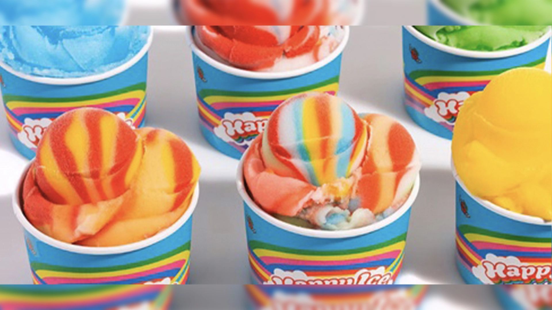 Colorful Cups of Rainbow Swirl Ice Cream Arranged in a Grid Bright Blue Wrappers with Rainbow Stripes Visible on Each Cup