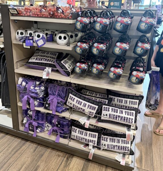 Display of Halloween themed Items on a Store Shelf Purple Gift Bags on the Lower Shelves White Skull Mugs on the Middle Shelf and Nightmare Before Christmas Pillows with Bold Text Reading'SEE YOU IN YOUR NIGHTMARES' on the right.